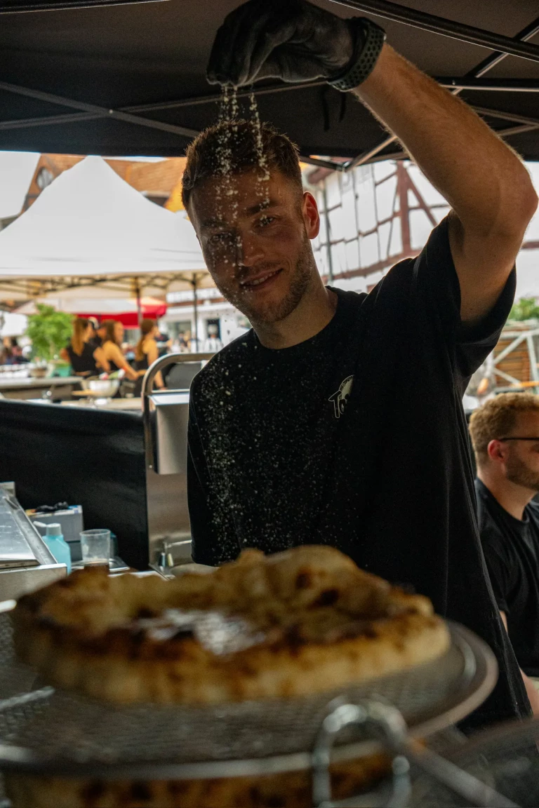 Pizzabäcker streut Parmesan über eine frisch gebackene Pizza