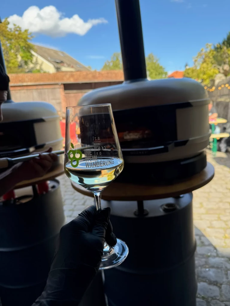 Weinglas der Weinwanderung vor dem mobilen Pizzaofen unter blauem Himmel